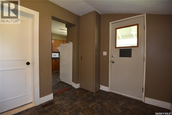 View from hallway showing a white door, a closet, a door to the exterior, and an opening to the kitchen. - 403 2nd Street W, Nipawin