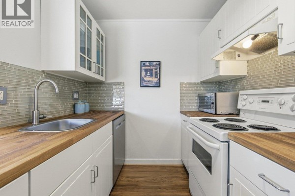 White kitchen with wood countertops, stainless steel refrigerator, and white appliances. - 403 570 E 8th Avenue, Vancouver