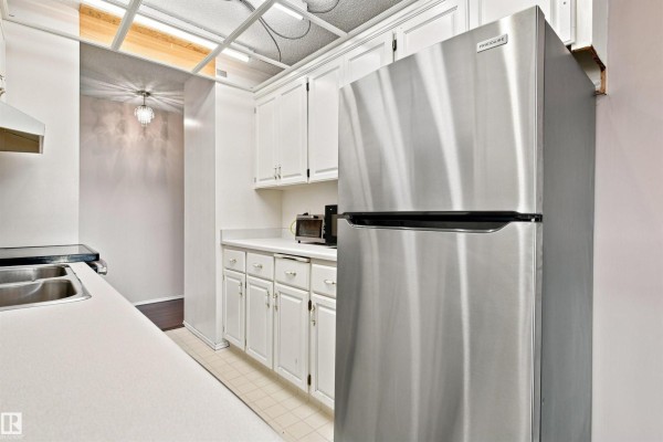 Galley kitchen featuring white cabinets, stainless steel refrigerator, and a toaster oven. - #403 9725 106 St Nw, Edmonton