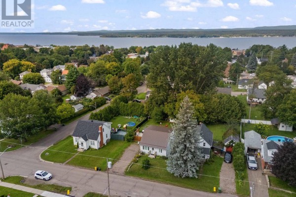 Aerial view of the grey house with a brown metal roof and neighboring properties, with a large lake in the background. - 403 Alfred Street, Pembroke