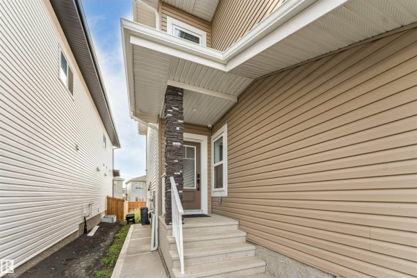 Side view of a modern house with tan and dark brown siding, white trim, and a beige garage door. - 403 Pine Point, Leduc