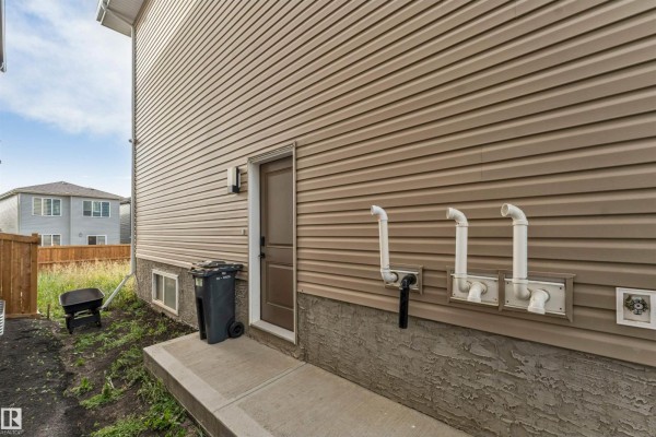 Front door steps and entrance of a tan house with stacked stone accents and white railings. - 403 Pine Point, Leduc