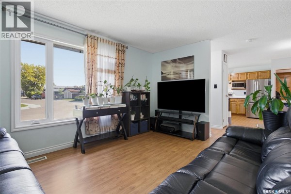 Living room with black leather sofa, large TV, wooden floors, and window view of the street. - 403 Sherry Crescent, Saskatoon