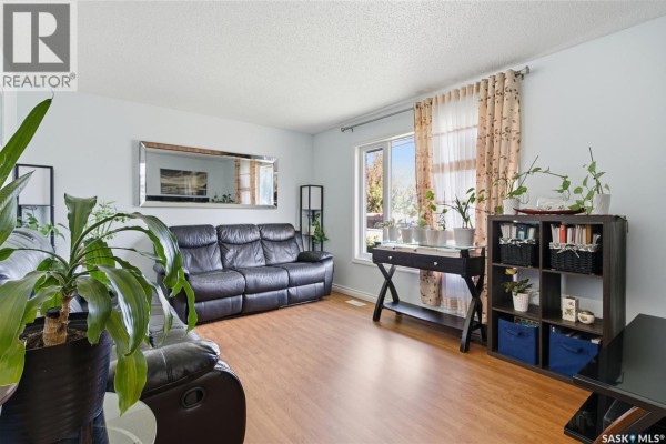 Living room with black leather sofa, large mirror, wooden floors, plants, and window view of the street. - 403 Sherry Crescent, Saskatoon