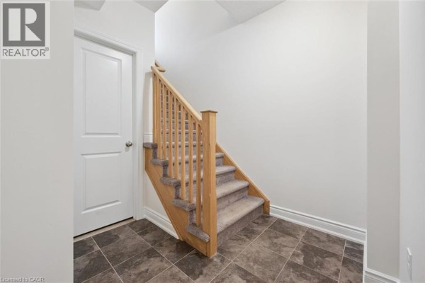 Interior hallway with a closed white door and a carpeted staircase with oak railings. - 403 Westwood Drive Unit# 16, Kitchener