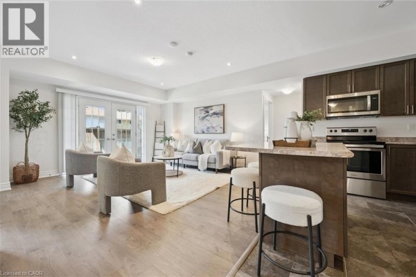 Open-concept living room and kitchen with a breakfast bar, stainless steel appliances, and French doors. - 403 Westwood Drive Unit# 16, Kitchener