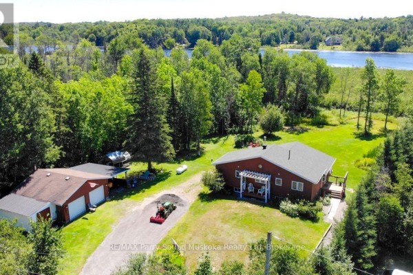 Side view of a red wood-sided house with a large deck and screened-in porch on a sunny day. - 4031 Highway 520 Highway, Magnetawan