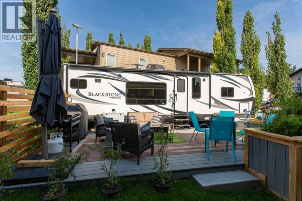 Deck with patio furniture, barbecue, and an umbrella next to a parked fifth-wheel RV. - 4034, 25054 South Pine Lake Road, Rural Red Deer County