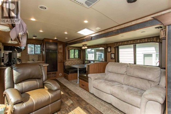 Interior view of a trailer living area with two sofas, a recliner, and a dining booth. - 4034, 25054 South Pine Lake Road, Rural Red Deer County