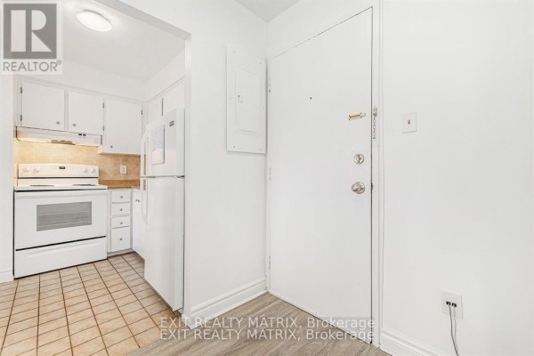 Hallway entrance to a kitchen with white appliances, white cabinets, and tiled floor. - 403c - 2041 Arrowsmith Drive, Ottawa