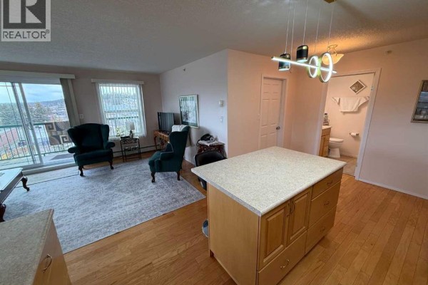 Living room with two green chairs, a balcony door, and a view of the hallway. - 404, 228 Pembina Avenue, Hinton