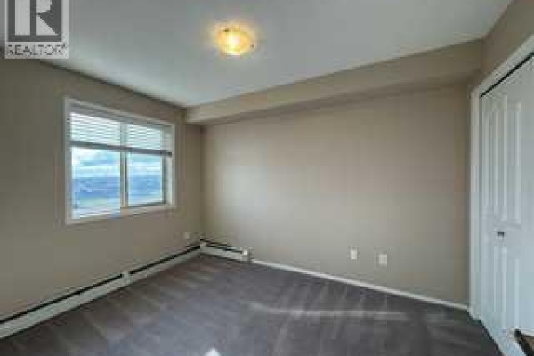 Bedroom with a window, beige walls, grey carpet, and a white closet. - 404, 7130 80 Avenue Ne, Calgary