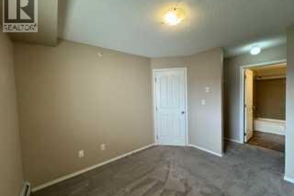 Bedroom with beige walls, grey carpet, and a white door leading to bathroom. - 404, 7130 80 Avenue Ne, Calgary