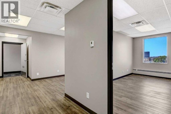 Office interior with light wood-look flooring, gray walls, and windows showing a city view. - 404, 9728 101 Avenue, Grande Prairie