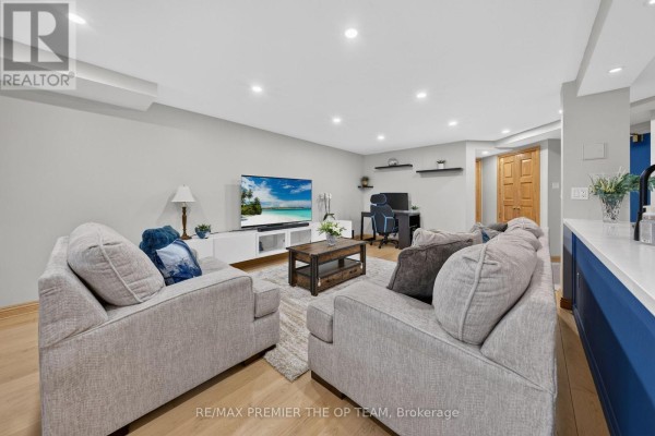 Living room with light gray walls, beige couches, wood floor, and television. - 404 - 100 Arbors Lane, Vaughan