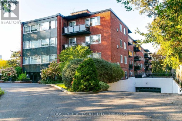 Side view of a red brick apartment building with balconies and a paved driveway leading to an underground garage. - 404 - 158 Crescent Road, Toronto