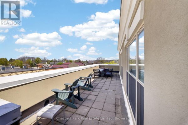 Large balcony with chairs and tables overlooking rooftops and distant trees. - 404 - 280 Main Street, Prince Edward County