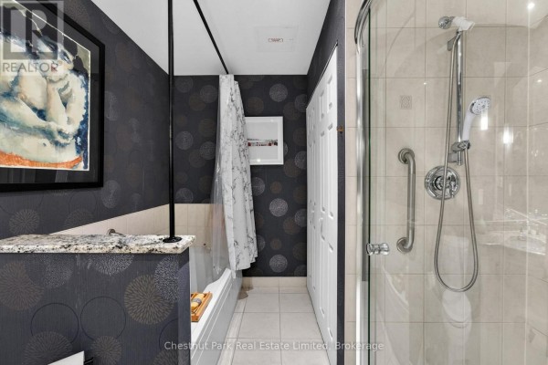 Bathroom with a bathtub, shower stall, white tile, and dark patterned wallpaper. - 404 - 280 Main Street, Prince Edward County