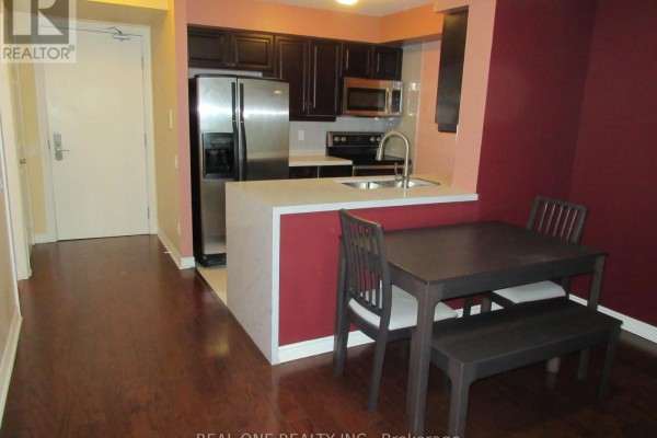 Kitchenette with dark wood cabinets, stainless steel appliances, and a small dining area. - 404 - 61 Town Centre Court, Toronto