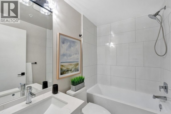 Modern bathroom with a white tub, tiled walls, toilet, and vanity with a large mirror. - 404 12143 223 Street, Maple Ridge