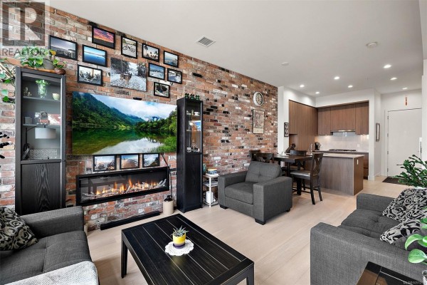 Living room showcasing a fireplace, entertainment unit, brick wall, and a view of the kitchen. - 404 1216 Carlisle Ave, Esquimalt
