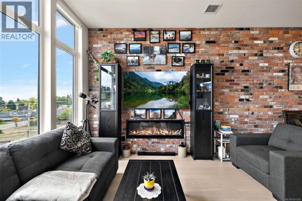 Living room with a sectional sofa, entertainment unit, fireplace, and windows overlooking the neighbourhood. - 404 1216 Carlisle Ave, Esquimalt