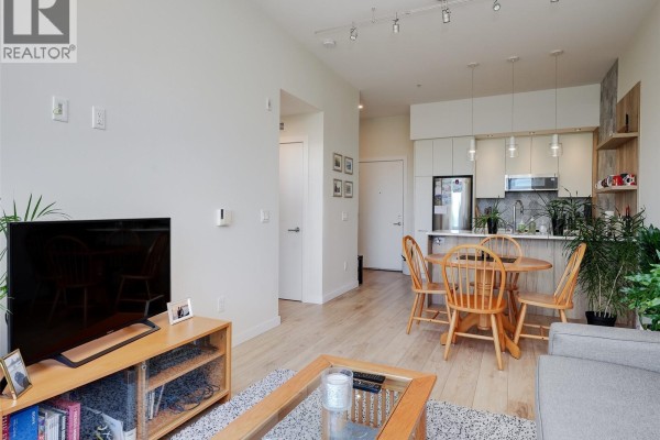 Living room with light wood floors, gray sofa, and open-concept kitchen. - 404 1588 North Dairy Rd, Saanich