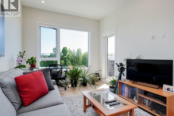 Living area with gray sofa, large window, and city views. - 404 1588 North Dairy Rd, Saanich