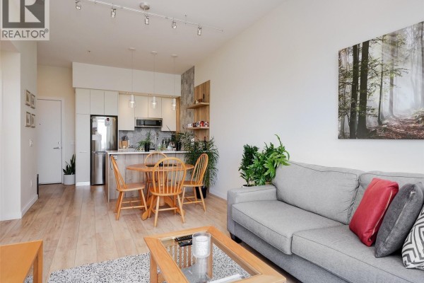 Living and dining area with light wood floors and modern kitchen. - 404 1588 North Dairy Rd, Saanich