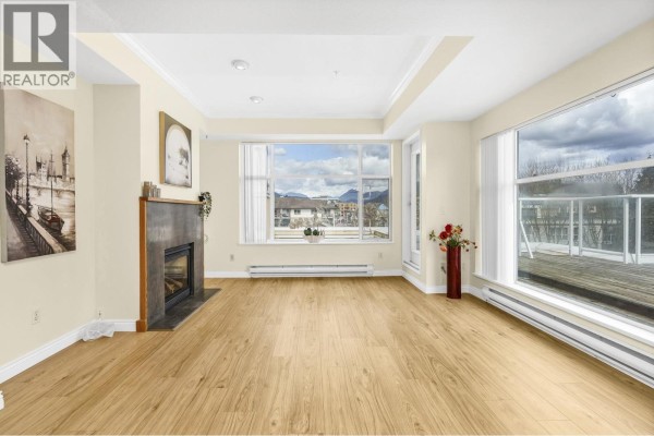 Living room with fireplace, light wood floors, beige walls, and view of outside. - 404 2340 Hawthorne Avenue, Port Coquitlam