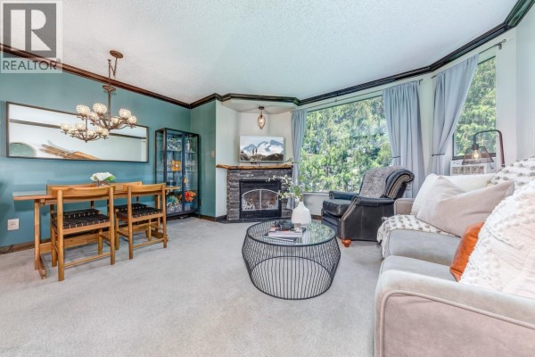 Living room with fireplace, dining table, sofa, and large window overlooking trees. - 404 4809 Spearhead Drive, Whistler