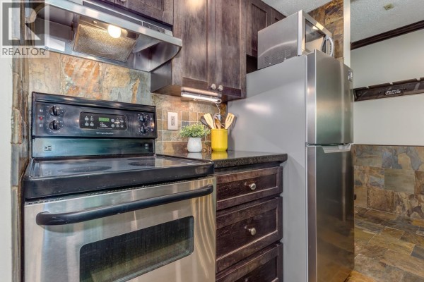 Kitchenette with dishwasher, sink, stone backsplash, and doorway to bathroom. - 404 4809 Spearhead Drive, Whistler