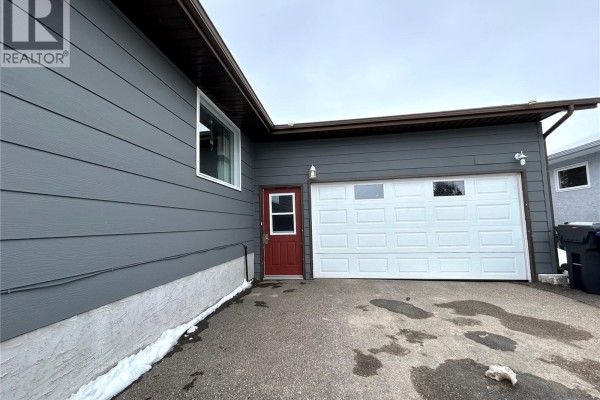 A detached garage with a white garage door is shown next to a residential house with grey siding. - 404 5th Street N, Nipawin