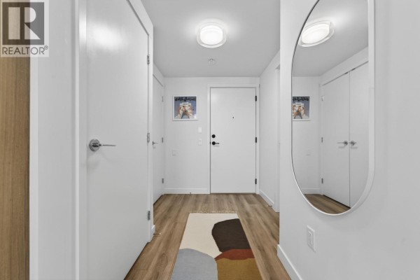 Apartment interior hallway with white doors, stacked washer and dryer, wood-look floor, and a rug. - 404 648 Lea Avenue, Coquitlam
