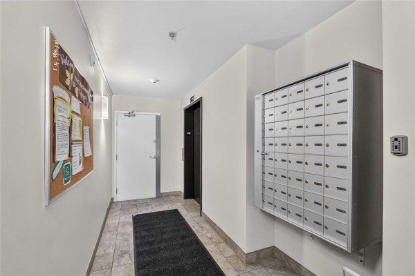 Apartment building hallway with a corkboard, mailboxes, and an elevator door. - 404 700 Allegheny Drive, Winnipeg