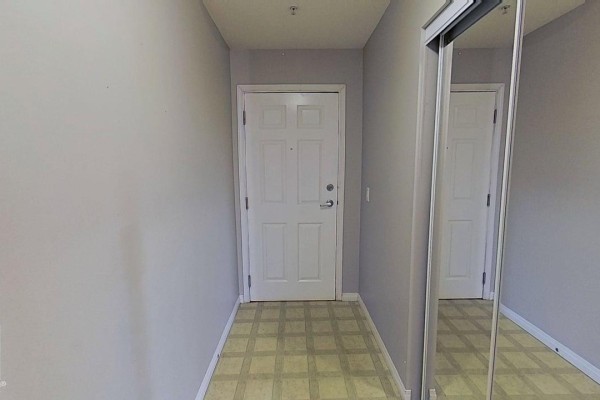 Apartment hallway with beige walls, a white door, and a mirrored closet. - #404 9945 167 St Nw, Edmonton