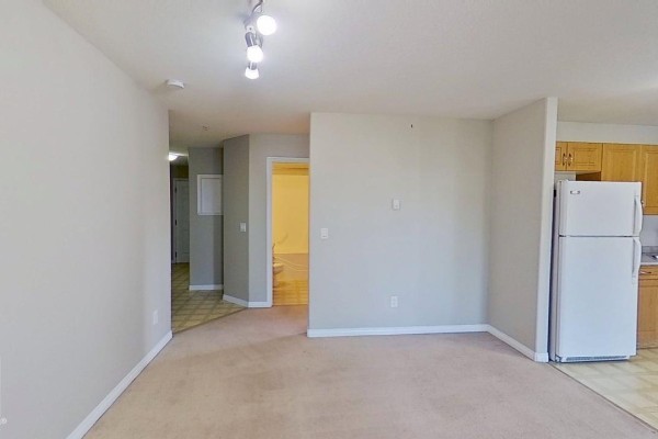 Living room with beige carpet, neutral walls, and an opening to the kitchen. - #404 9945 167 St Nw, Edmonton