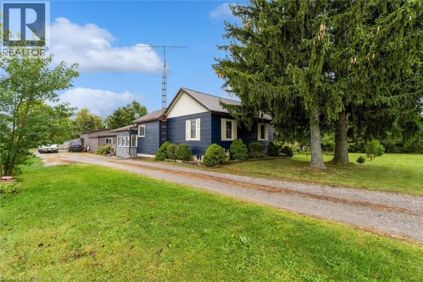 Side view of blue siding house with gravel driveway, green lawn, and mature trees. - 404 Concession 5 Road, Fisherville
