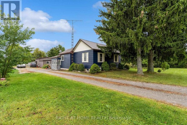 Side view of a blue house with a metal roof, large windows, and surrounding green lawn. - 404 Concession 5 Road, Haldimand