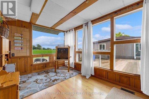 Sunroom with wood paneling, large windows with white curtains, wooden beams, and views of the backyard. - 404 Concession 5 Road, Haldimand