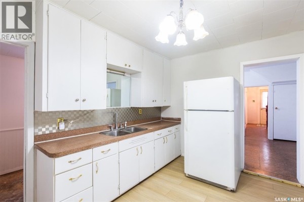 A white kitchen with white cabinets, double sink, and a large white refrigerator. - 404 Fairford Street W, Moose Jaw