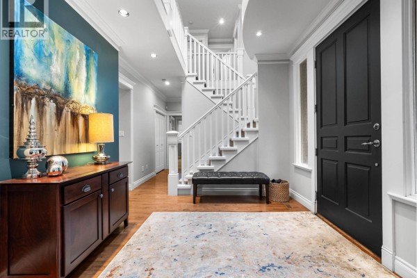 Spacious entryway with dark wood front door, wood floor, and staircase. - 4047 Woodbury Avenue, North Vancouver