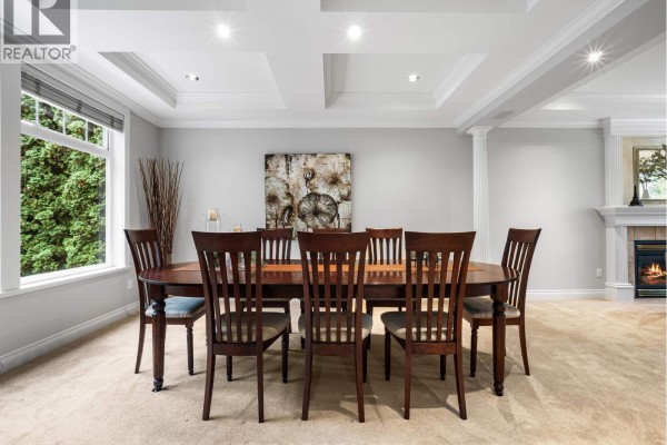 Formal dining room with a large wooden table, chairs, and a fireplace. - 4047 Woodbury Avenue, North Vancouver