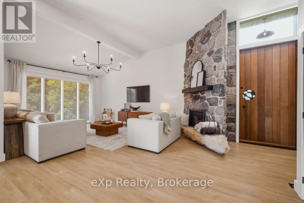Living room with a stone fireplace, wooden door, and light wood flooring. - 40481 Howick-turnberry Road, Morris Turnberry