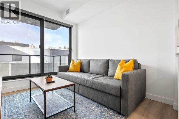 A white kitchen with stainless steel appliances, a large island, and light wood flooring. - 405, 123 4 Street Ne, Calgary