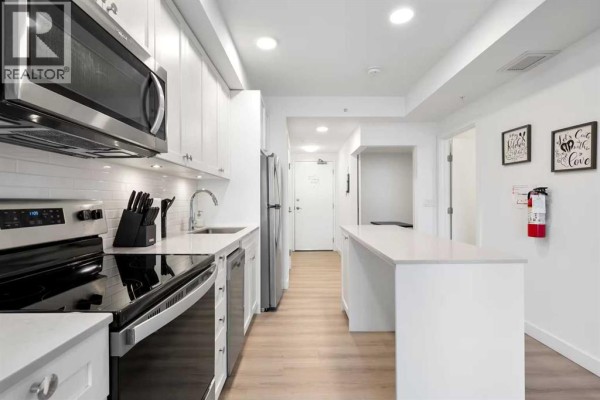 White kitchen with stainless steel appliances, subway tile backsplash, and a long island. - 405, 123 4 Street Ne, Calgary