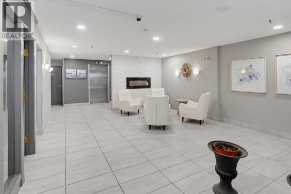 Apartment building lobby with white chairs, a fireplace, and tiled floors. - 405, 540 18 Avenue Sw, Calgary