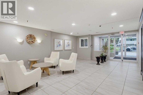 Apartment building lobby seating area with white chairs and decorative wall art. - 405, 540 18 Avenue Sw, Calgary