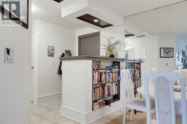 Interior hallway with built-in bookshelves and a dining area with chairs visible. - 405, 540 18 Avenue Sw, Calgary