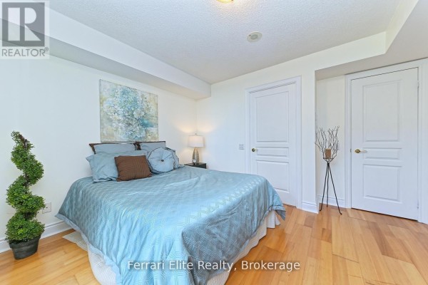 Bedroom with a queen-sized bed, blue bedding, hardwood floors, and two white doors. - 405 - 10 Northtown Way, Toronto